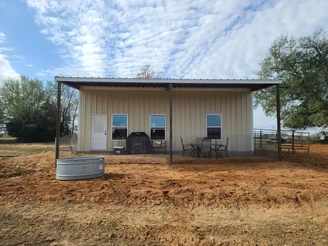 A small white house with a porch is sitting in the middle of a field.