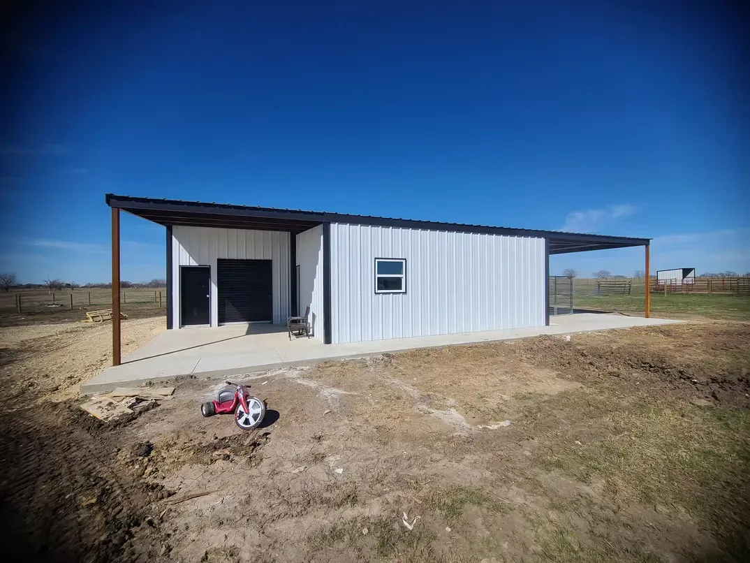 A white metal building with a porch and a red atv parked in front of it.