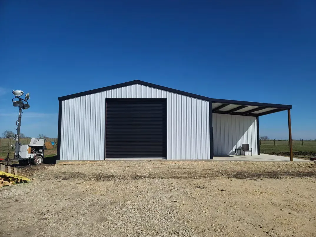 A white metal building with a black door is sitting in the middle of a dirt field.