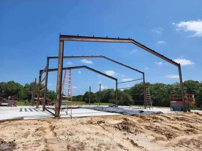 A large metal structure is being built in the middle of a dirt field.