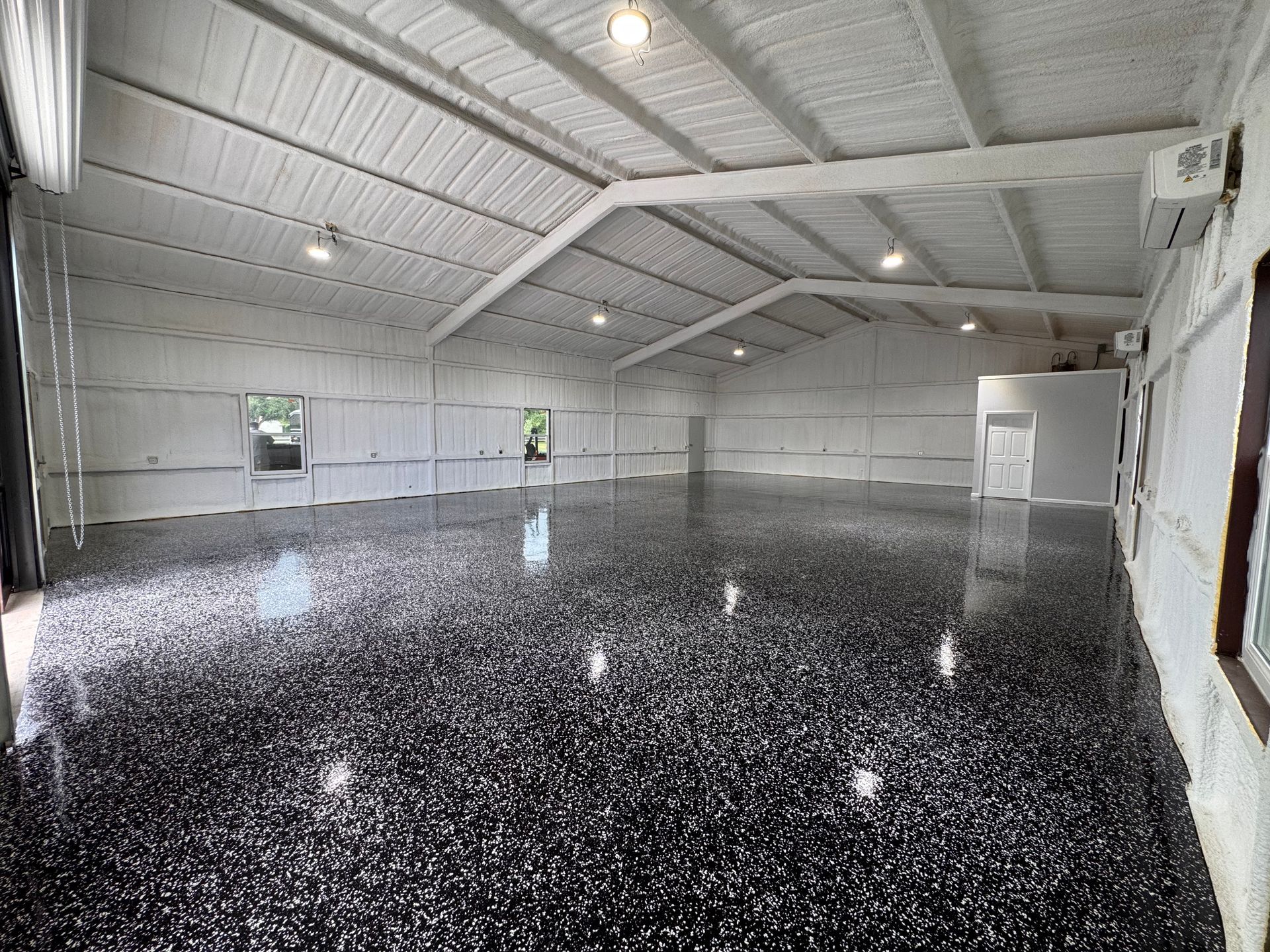 Spacious room with black speckled floor, white walls and ceiling, empty.