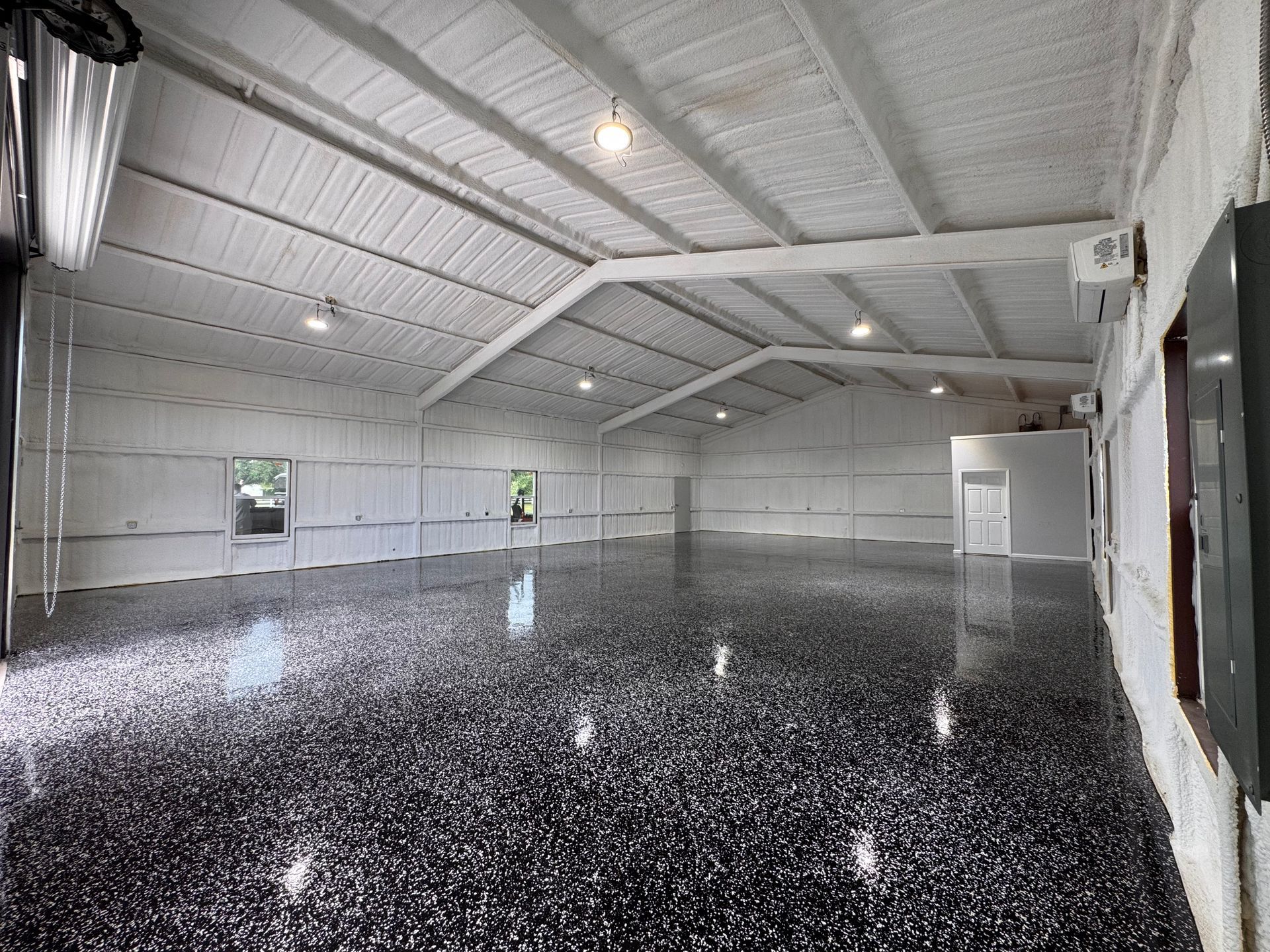 Large, empty, modern workshop with black speckled epoxy floor, white walls and ceiling.