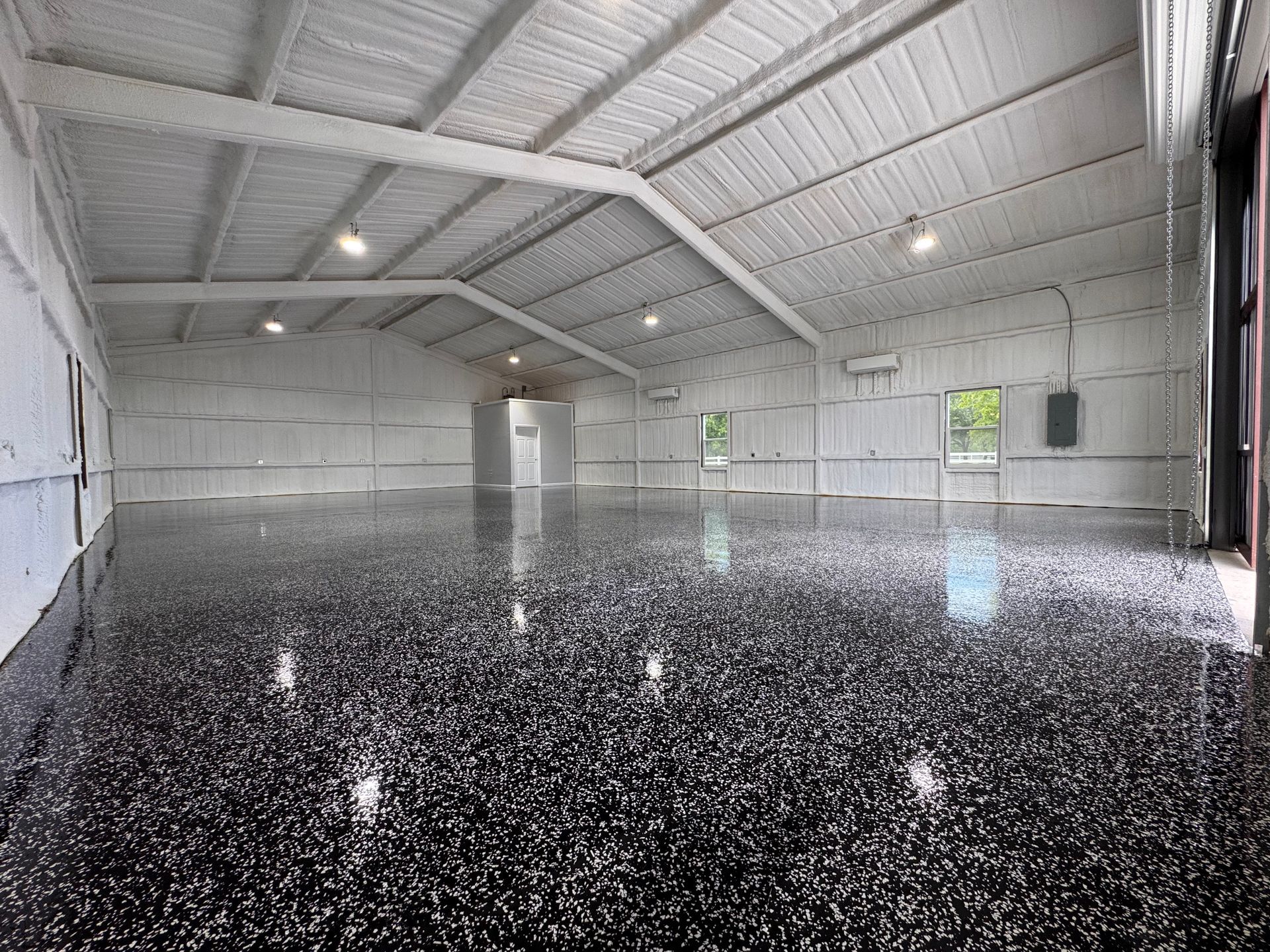 Inside a large, empty warehouse with a reflective, speckled black floor and white walls and ceiling.