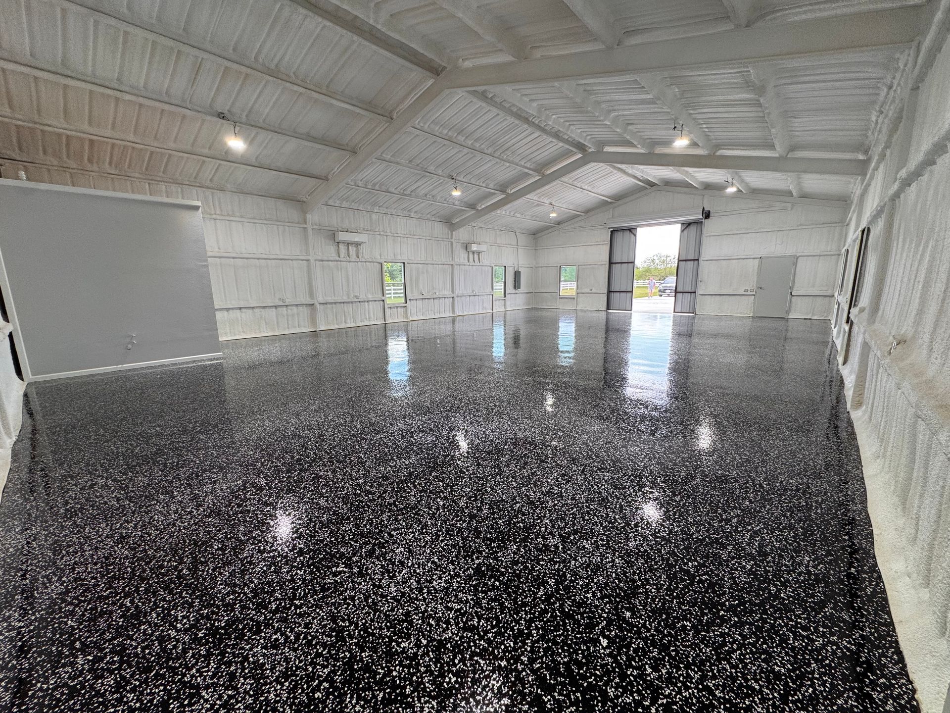 Shiny black epoxy floor in an open building, white walls and ceiling, large door open at far end.
