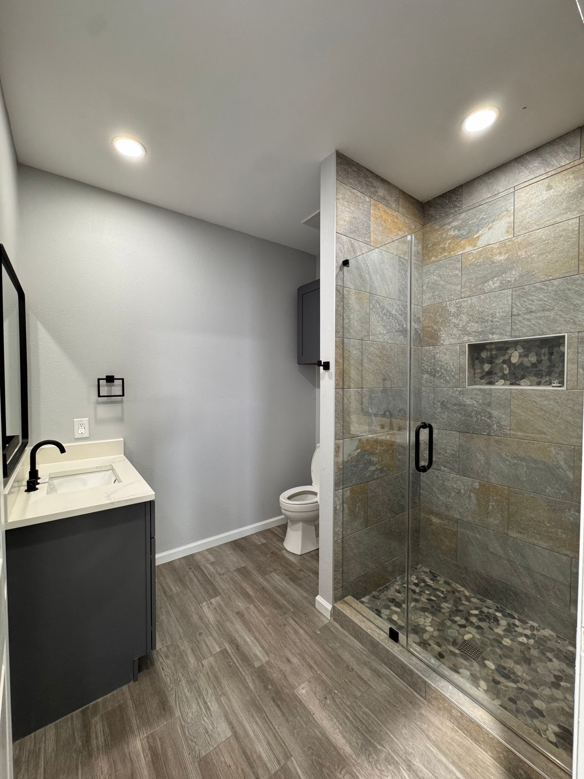 Bathroom with a gray vanity, tile shower, and wood-look flooring.