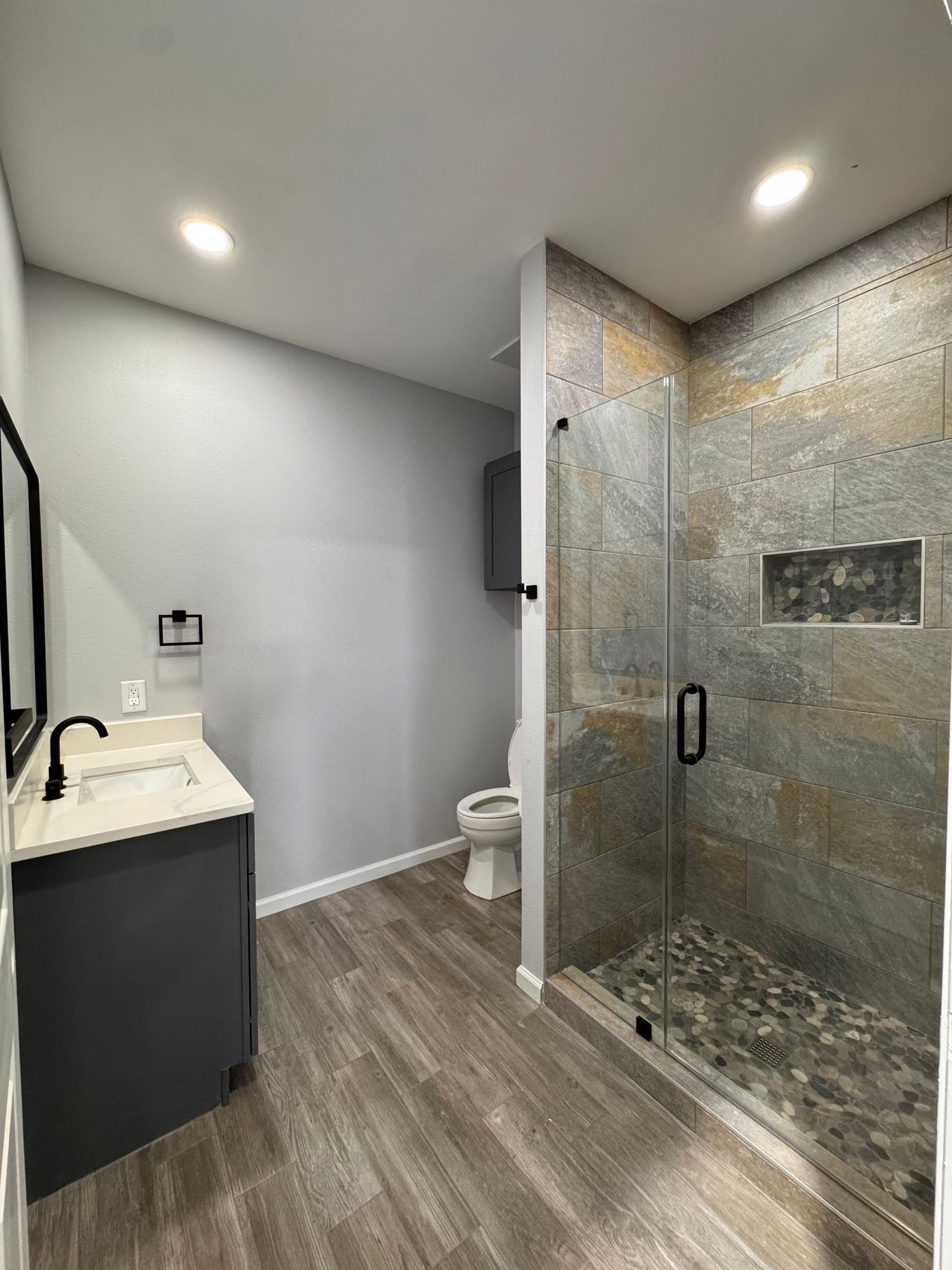 Bathroom with gray vanity, stone shower, and wood-look floors.