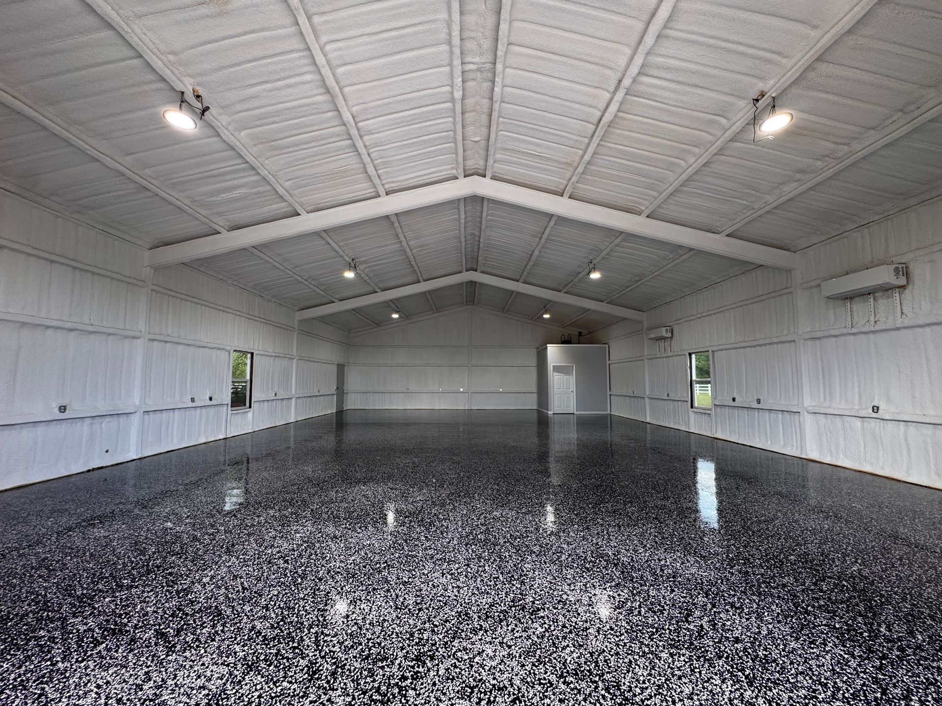 Inside a large, empty, white building with a shiny, speckled black floor; overhead lighting.