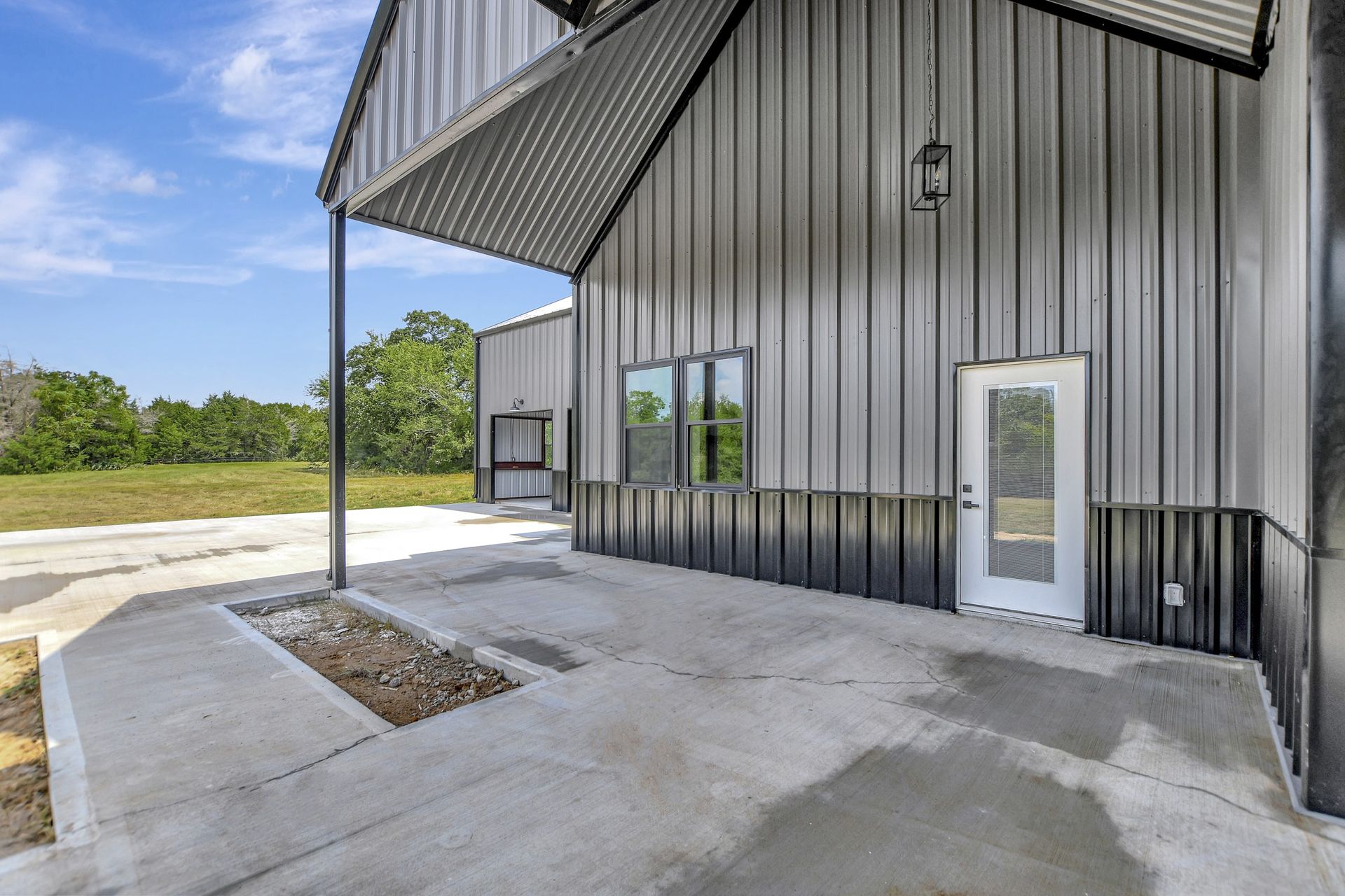 Metal building with a patio and an open roof, next to a grassy field and blue sky.