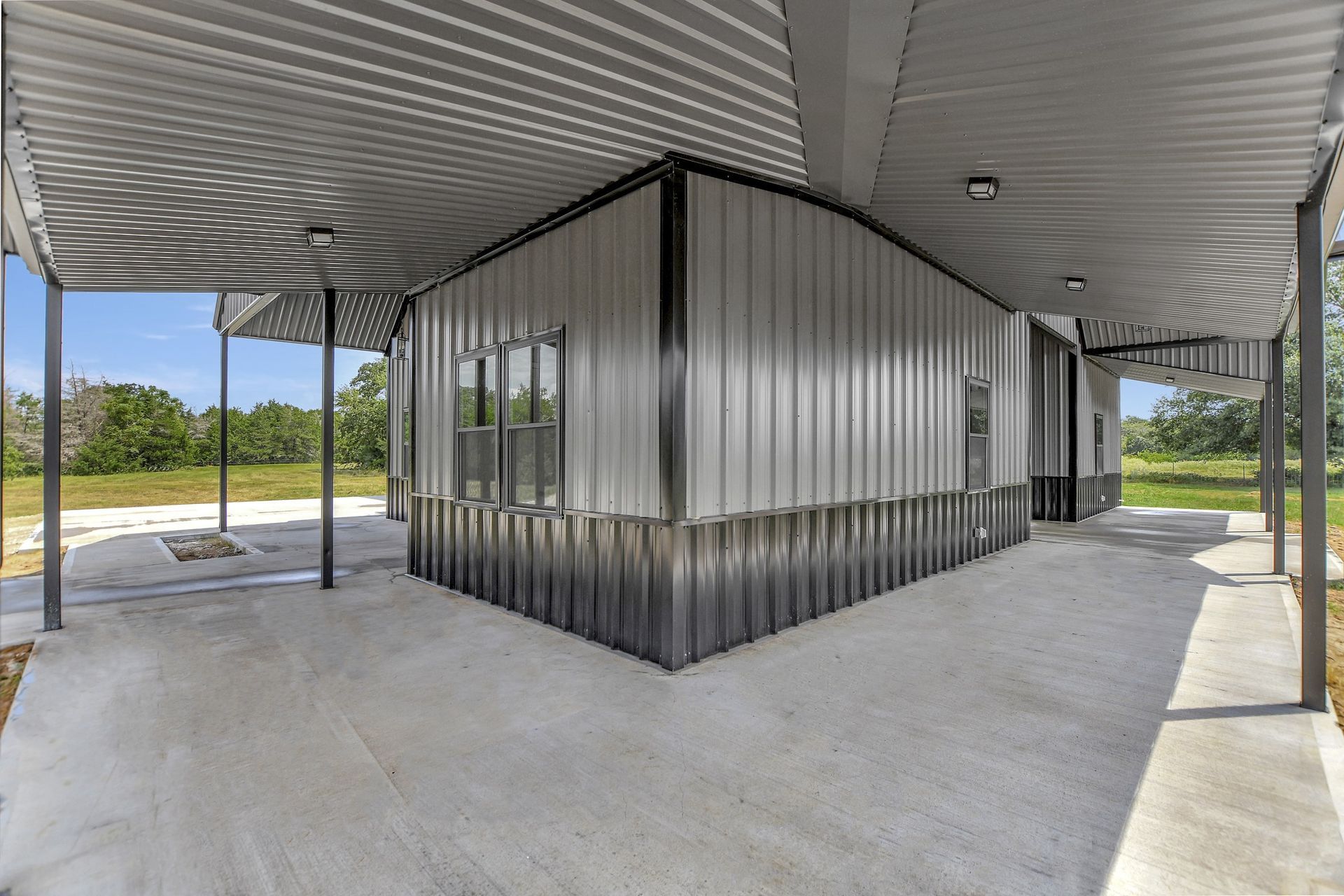 Metal building with covered walkways, concrete flooring, and a grassy field in the background.