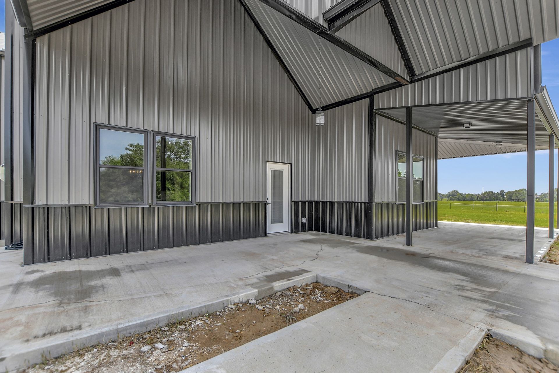 Metal-sided building with a concrete patio and covered porch. Exterior features black and silver colors.
