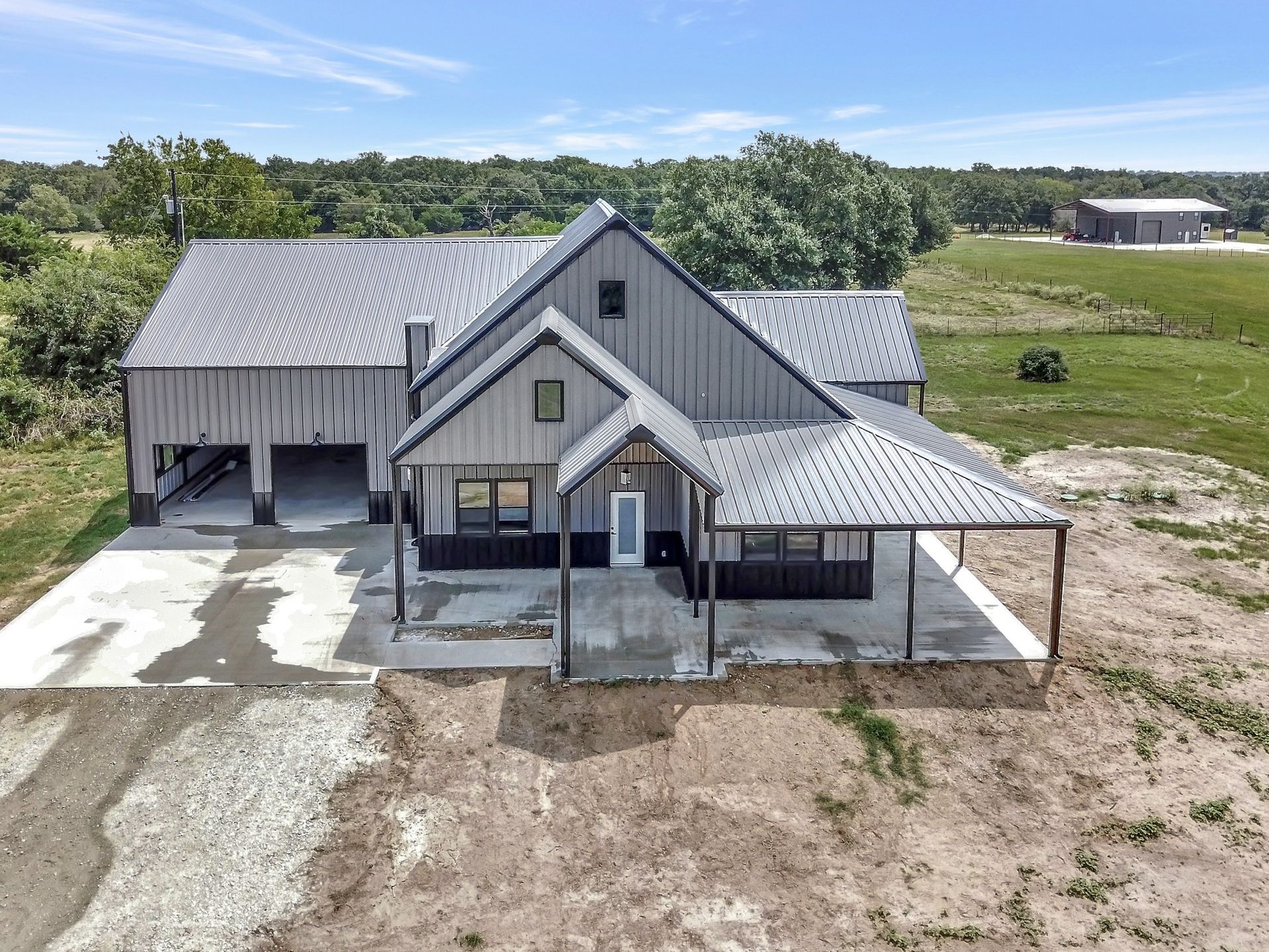 Modern farmhouse with gray metal roof, black siding, and open garage on a rural property.