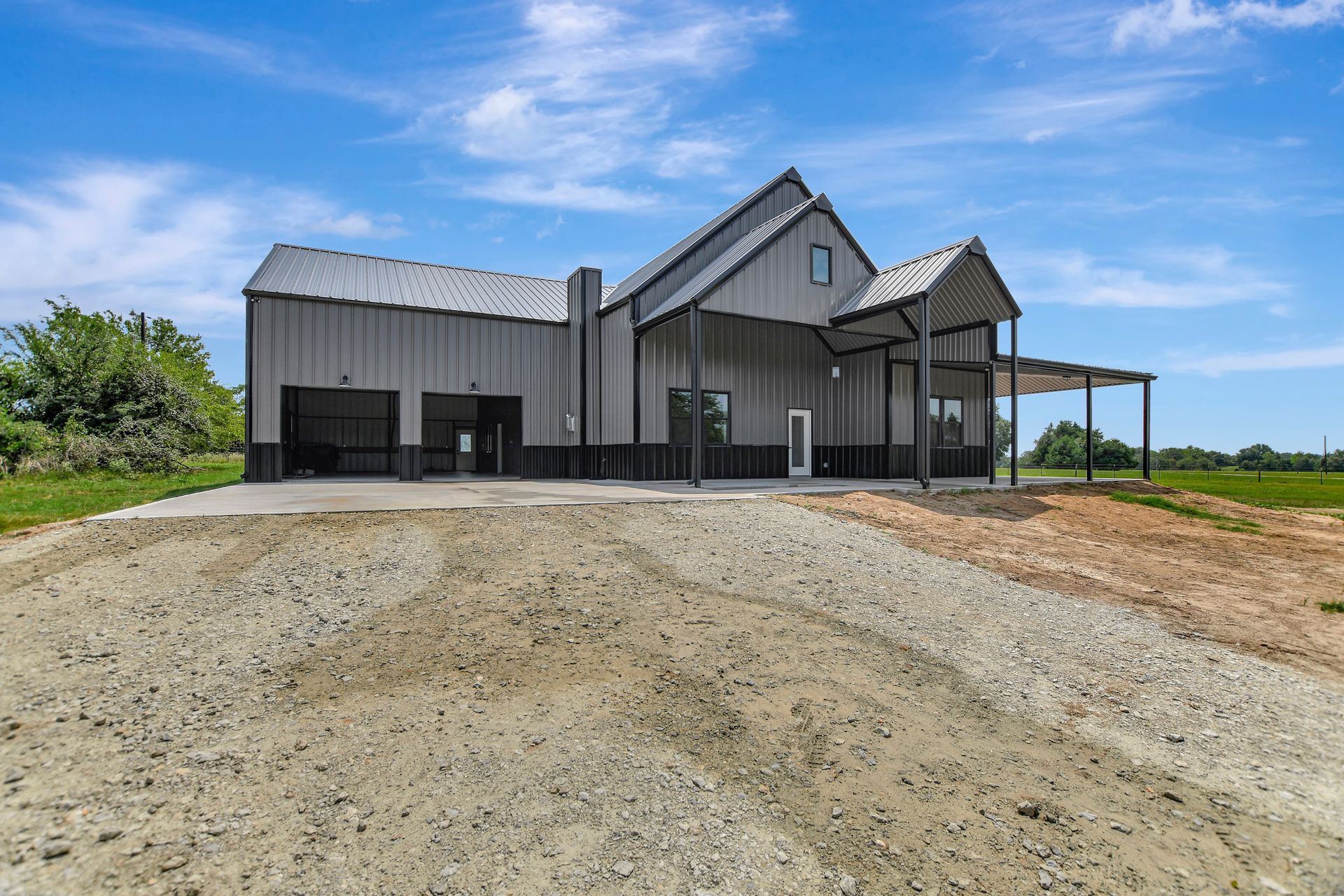 Gray barn-style house with a gravel driveway under a blue sky.