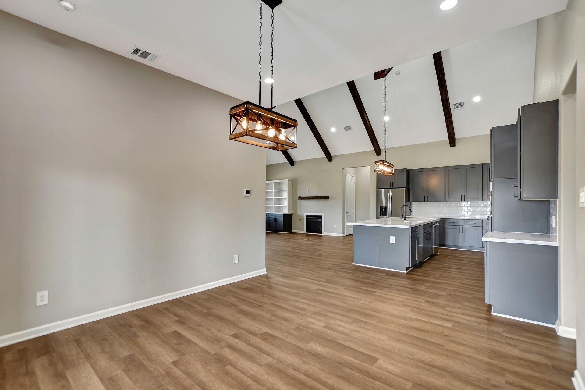 Open-concept kitchen and dining area with wood floors, gray cabinets, and rustic light fixtures.