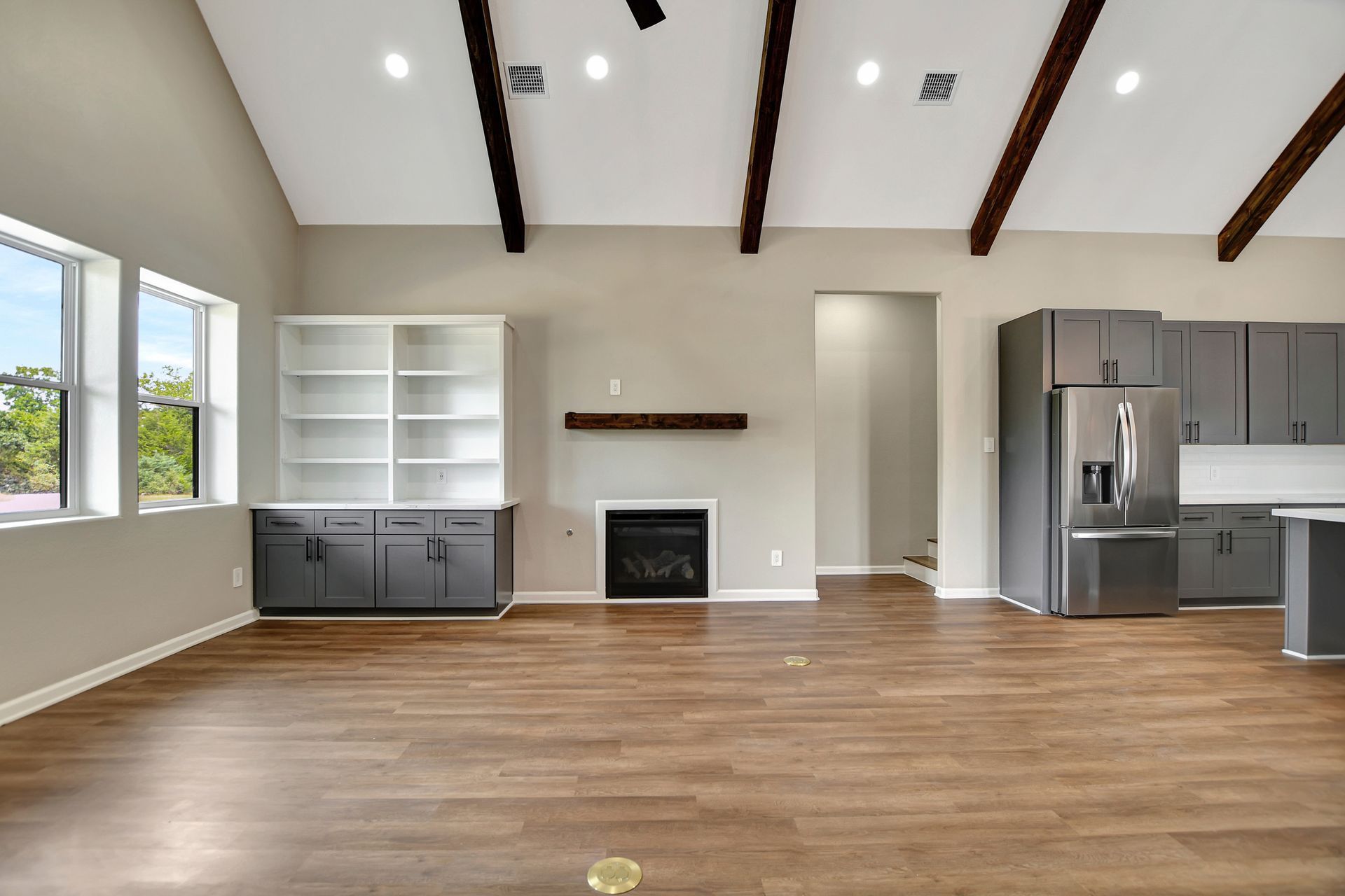 Modern living room with gray cabinets, fireplace, wood beams, and hardwood floors.