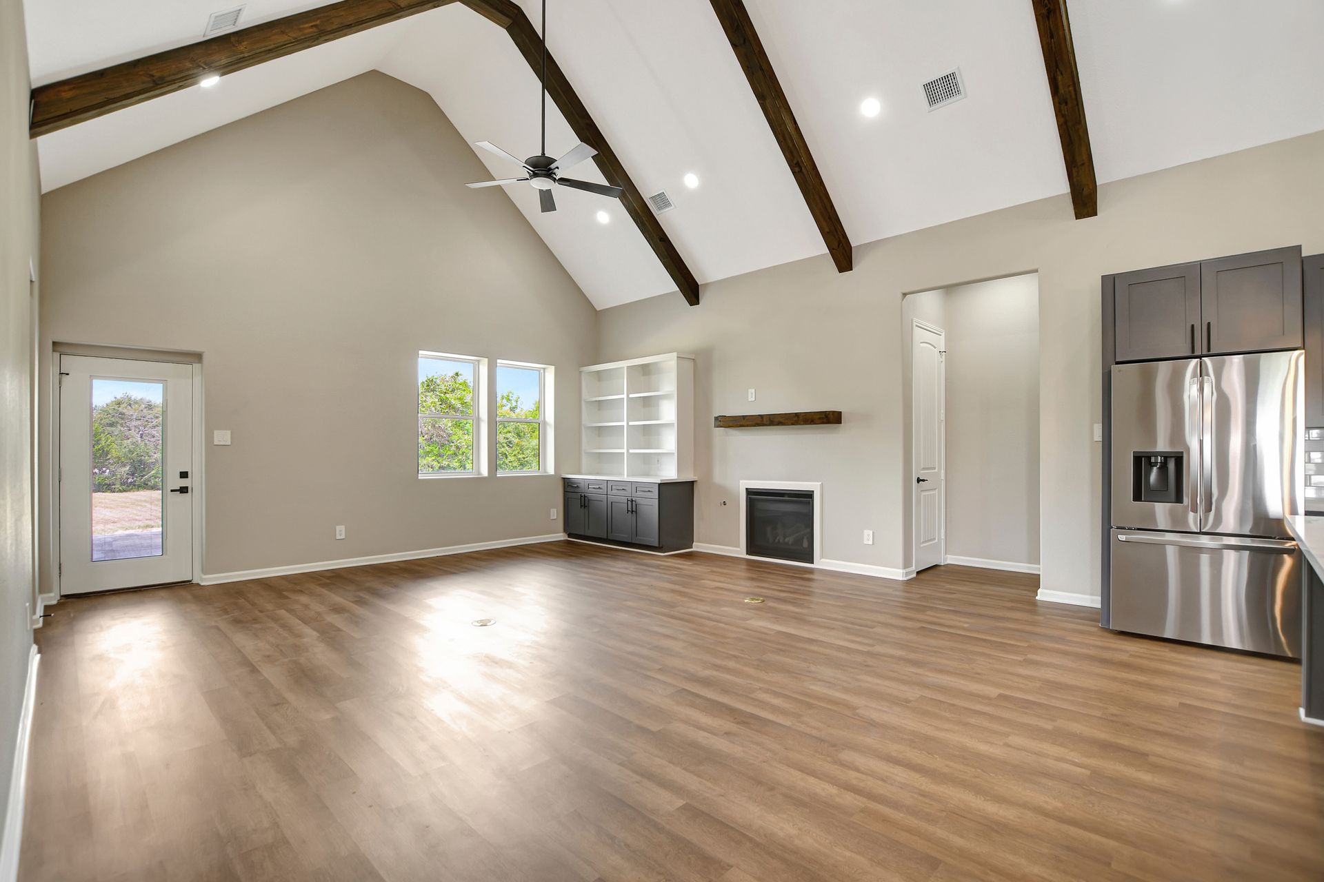 Empty modern living room with vaulted ceiling, wooden beams, and a fireplace.