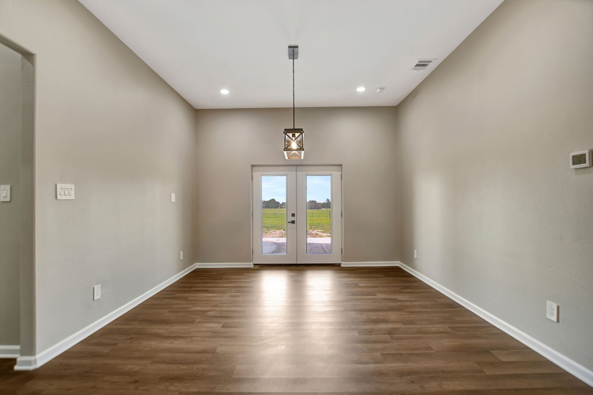 Empty dining room with wood flooring, light gray walls, and glass doors to a backyard.