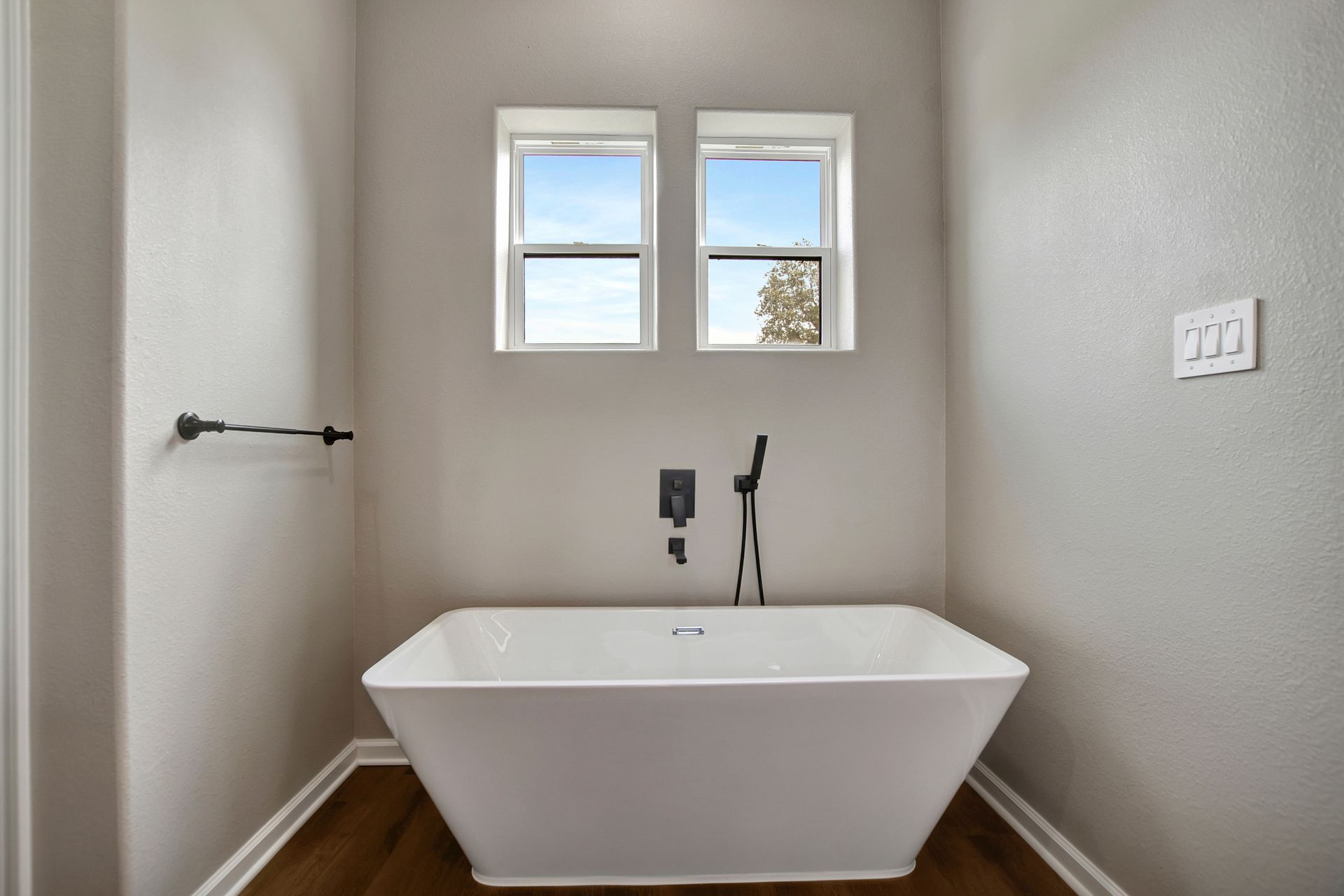 Modern bathroom with white tub, black fixtures, and two windows.