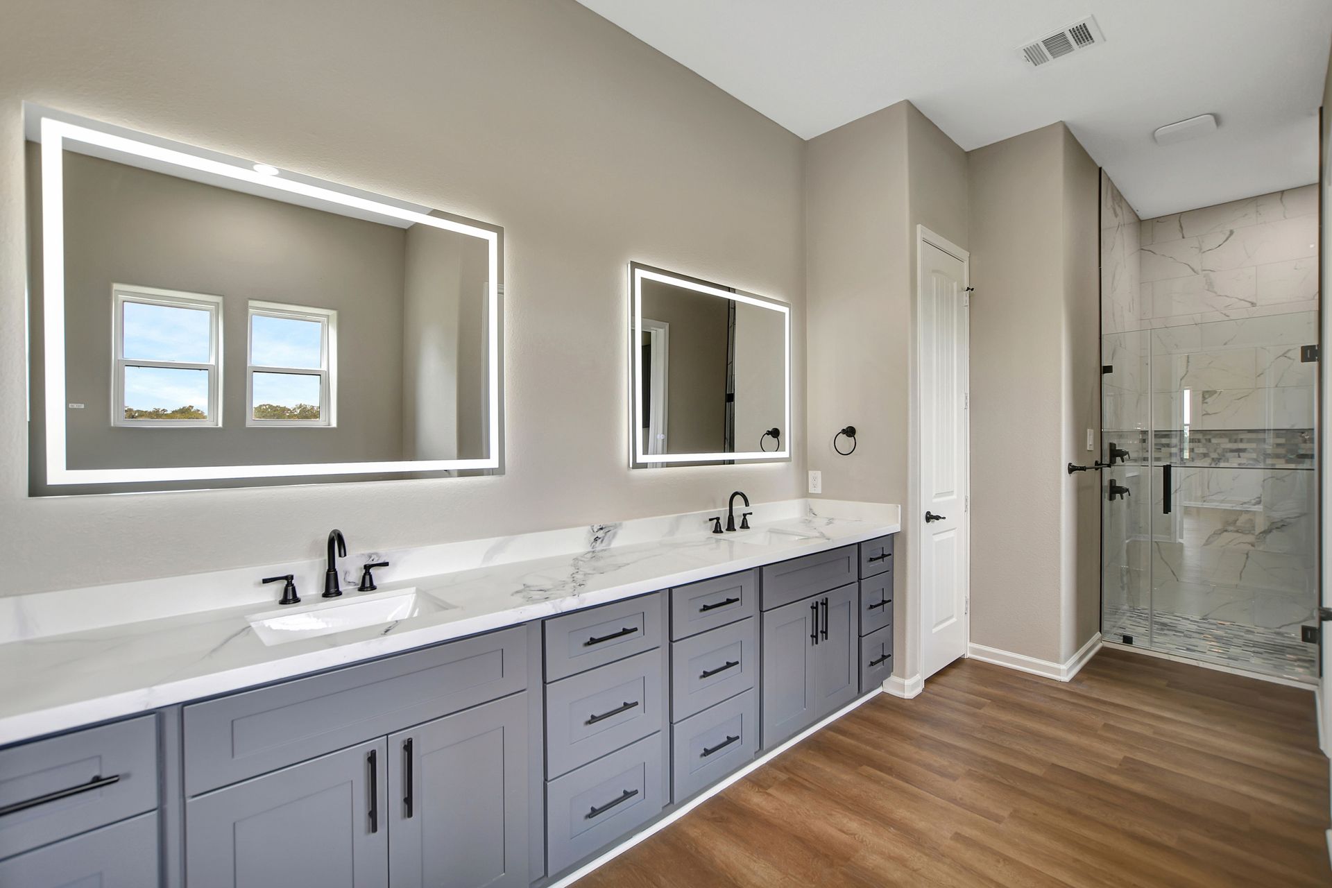 Modern bathroom with gray cabinets, marble countertops, and led mirrors.