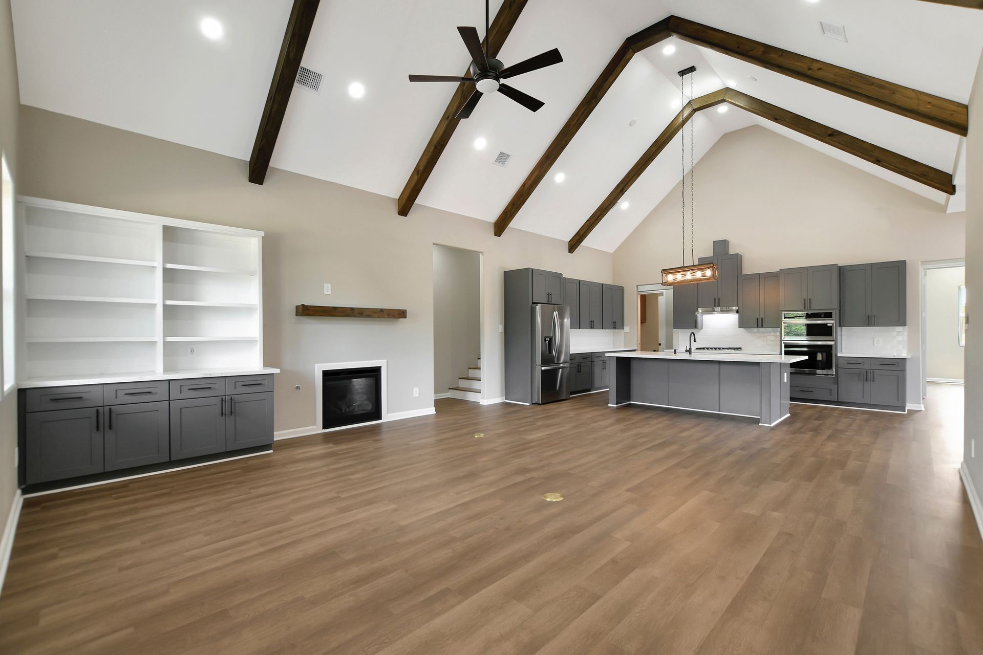 Spacious living area with vaulted ceiling, wood beams, gray kitchen cabinets, and fireplace.