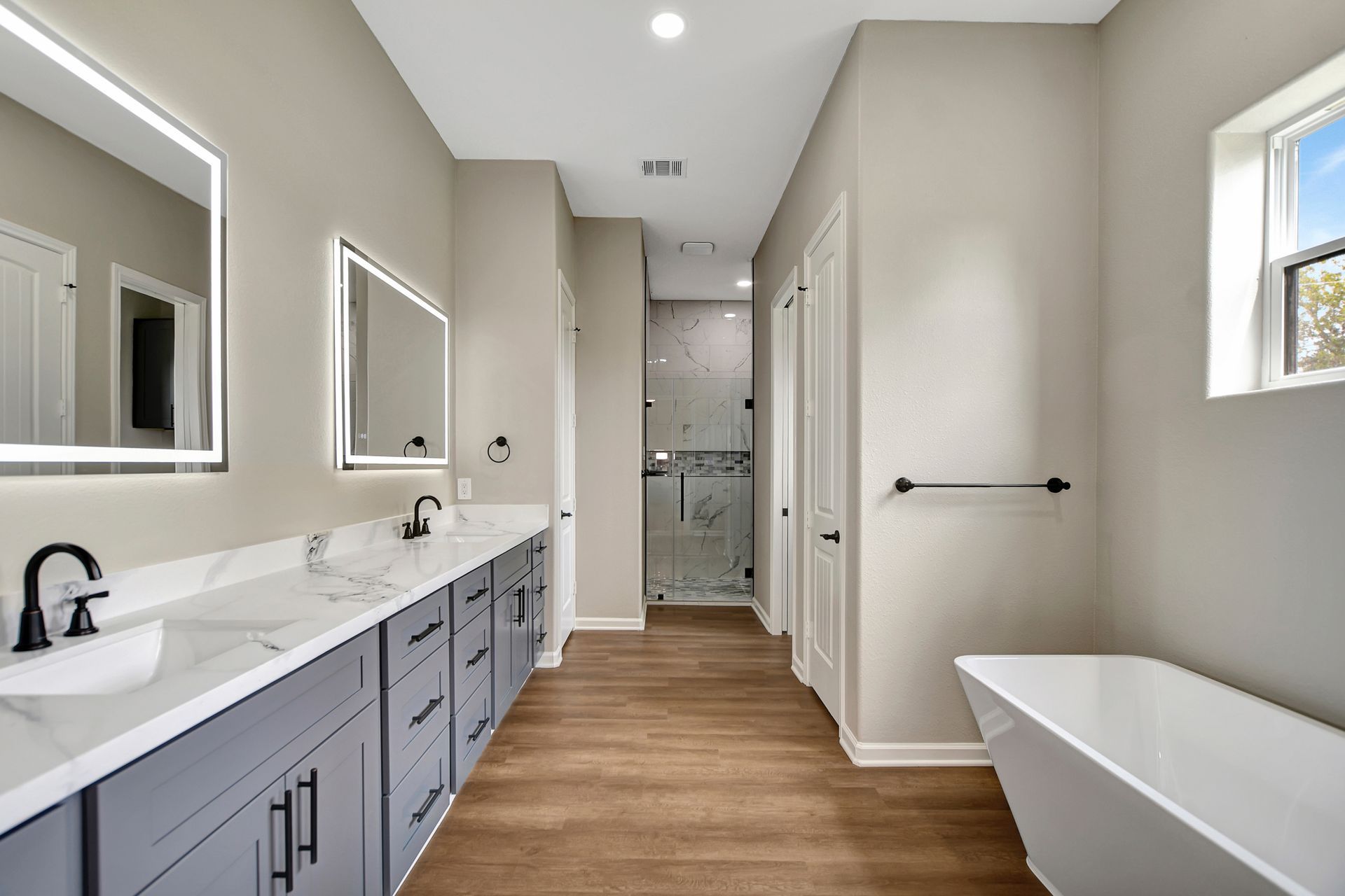 Spacious bathroom with double vanity, gray cabinets, freestanding tub, and walk-in shower.
