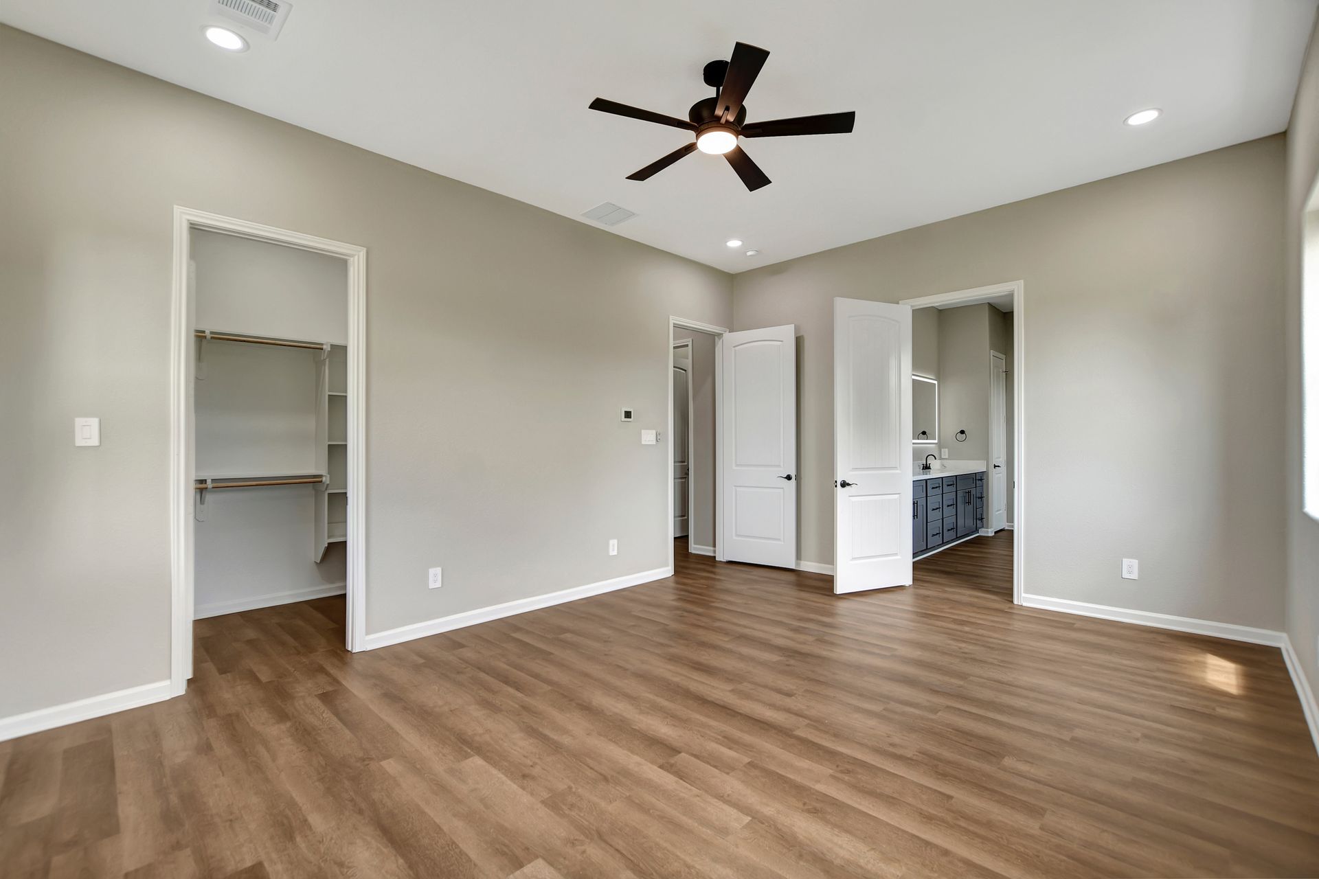 Bedroom with wood floor, neutral walls, walk-in closet, and bathroom door. A ceiling fan is installed.