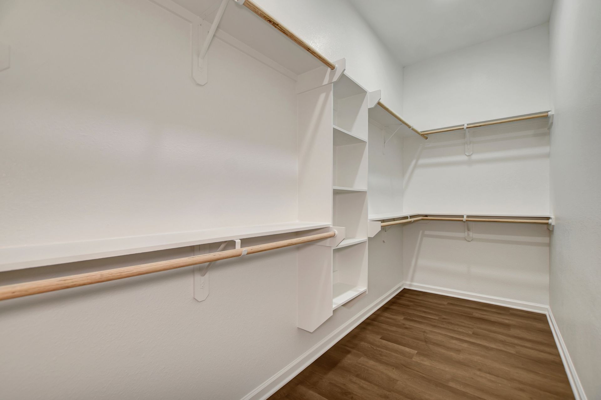 Empty, white walk-in closet with wooden shelves and floors.