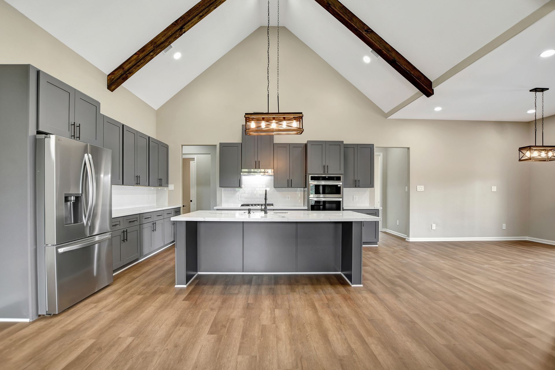 Modern kitchen with gray cabinets, island, wooden beams, and wood floors.
