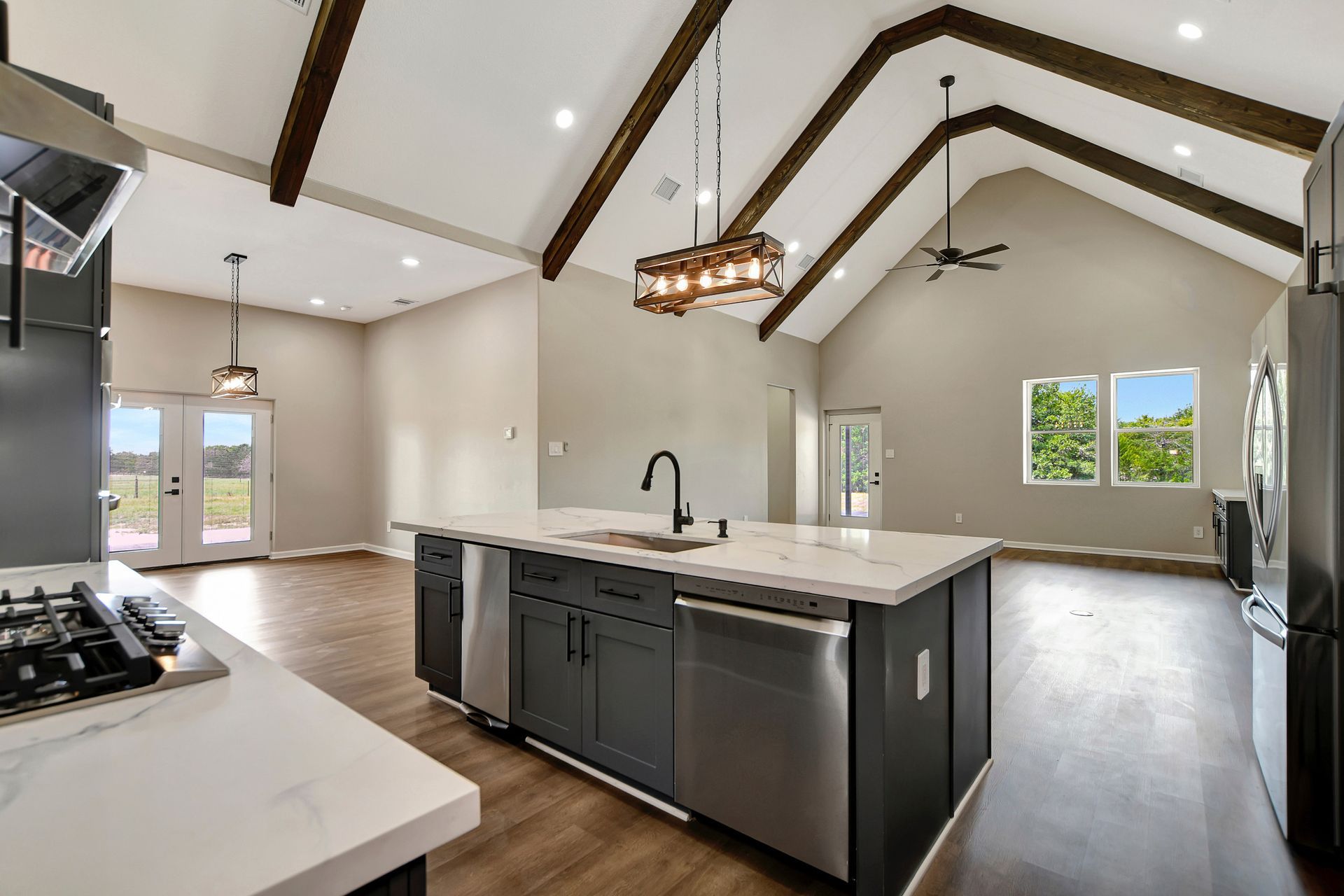 Open-concept kitchen with island, vaulted ceiling, wooden beams, and stainless steel appliances.