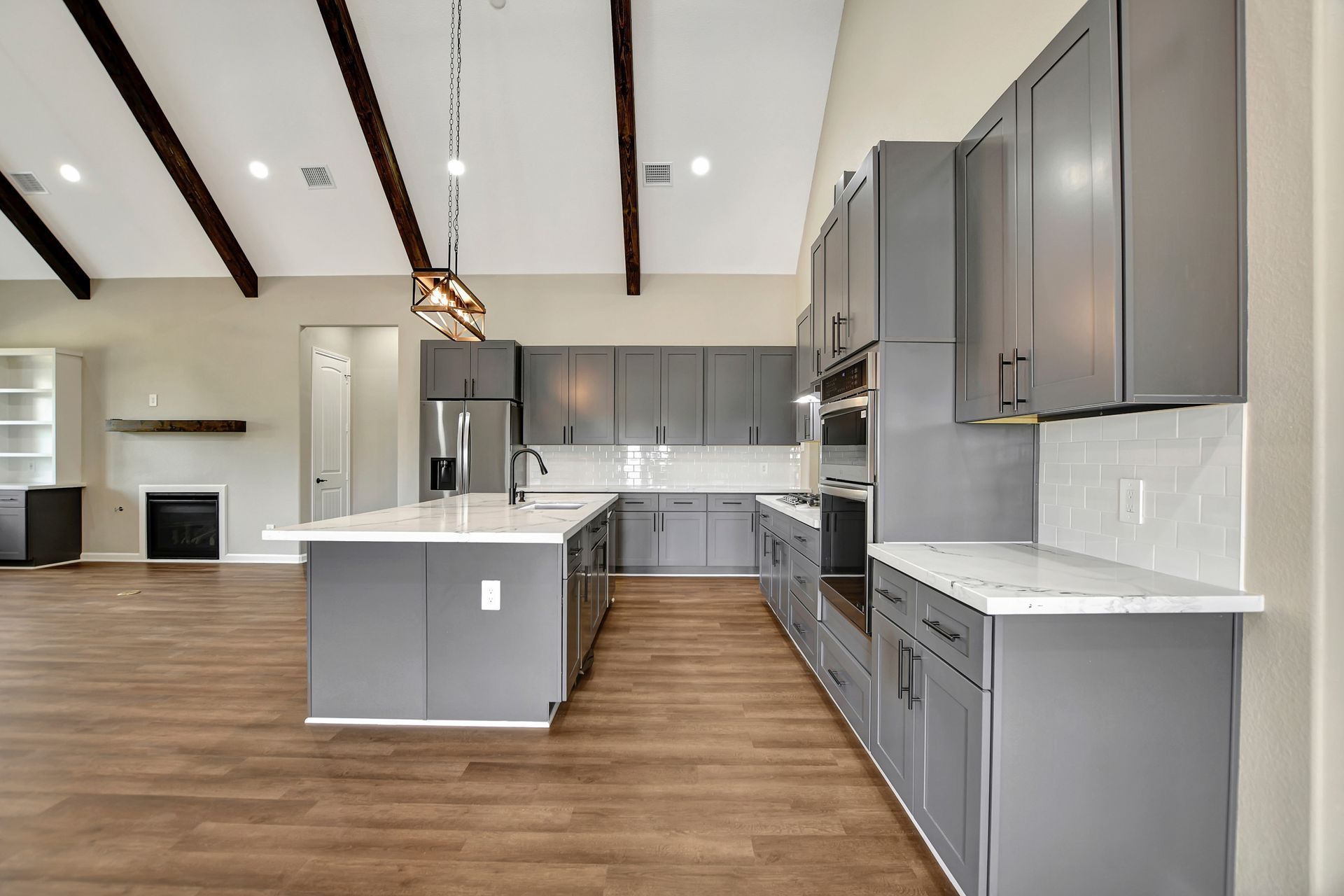 Modern gray kitchen with island, white countertops, wood beams, and wood-look flooring.