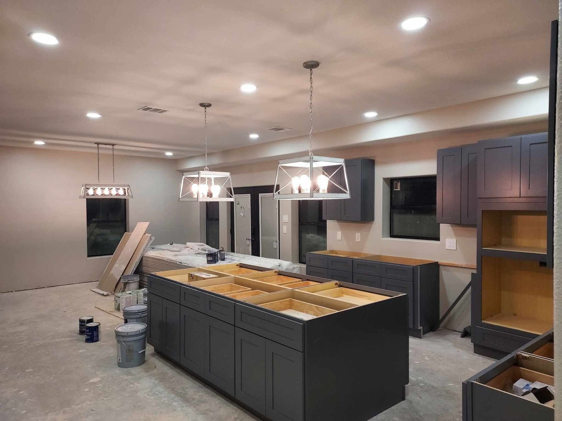 Kitchen renovation in progress, featuring gray cabinets, central island, pendant lights, and recessed lighting.