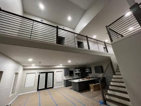 Interior view of a modern two-story home with a loft and black metal railings. Kitchen and stairs are visible.