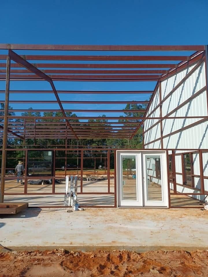 Steel-framed building under construction with metal siding and a concrete floor. White doors stand nearby.