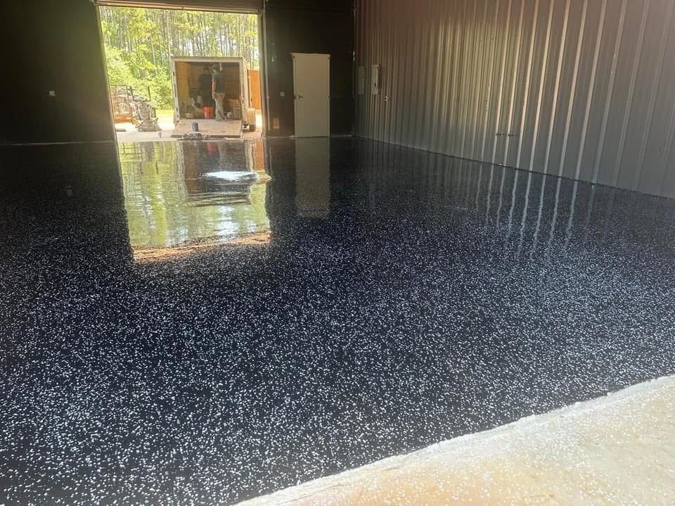 Shiny black speckled epoxy floor inside a building, reflecting the open doorway.