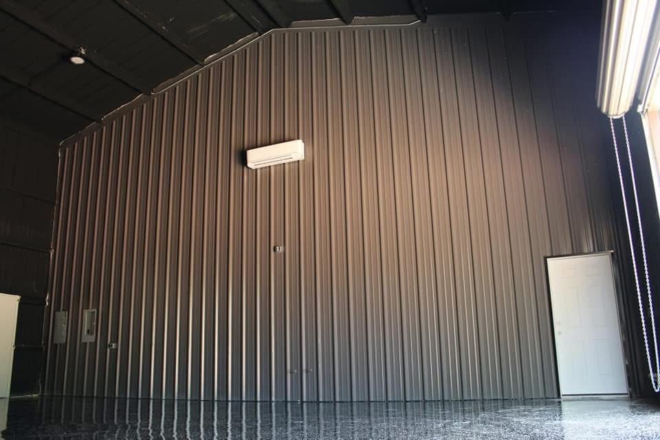 Interior of a dark gray metal building. A white door and air conditioner are on the wall.