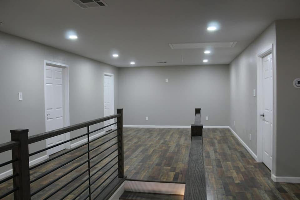Interior view of a renovated room with gray walls, wood floors, and a railing. White doors are visible.