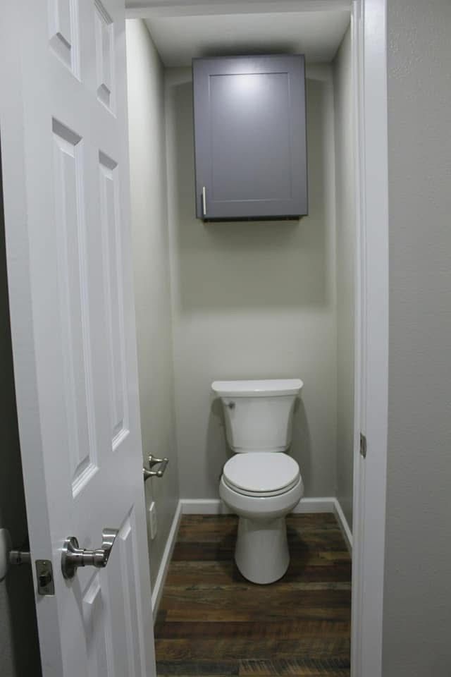 Small bathroom with a toilet and cabinet above, with a door on the left.