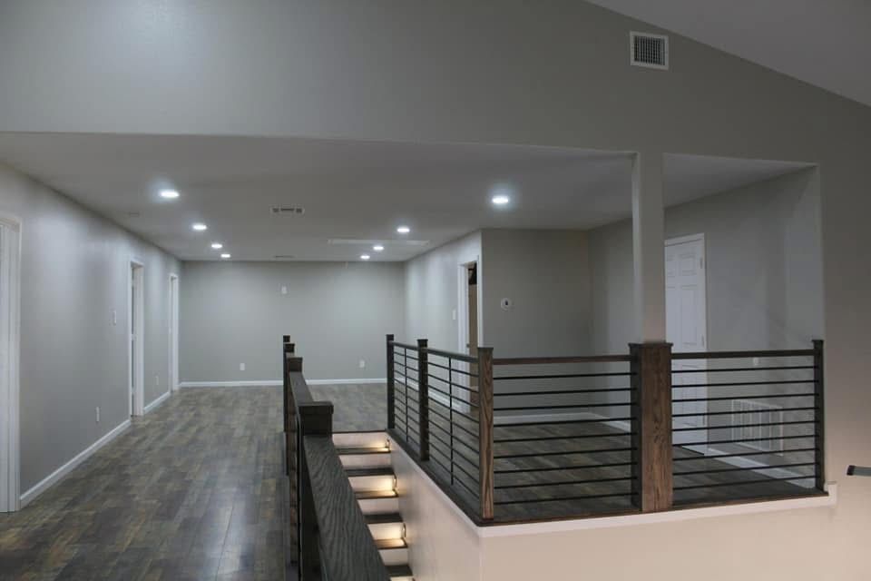 Interior view of a modern home, looking from a second-floor balcony. Features gray walls, wood flooring, and a black railing.