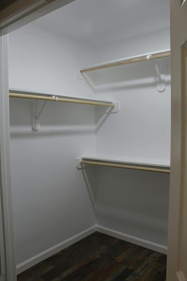 Empty white closet with three shelves and a hanging rod, with a dark wood floor.