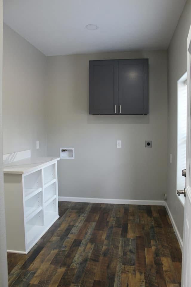 Laundry room with gray walls, wood-look floor, white countertop, and dark gray cabinets.