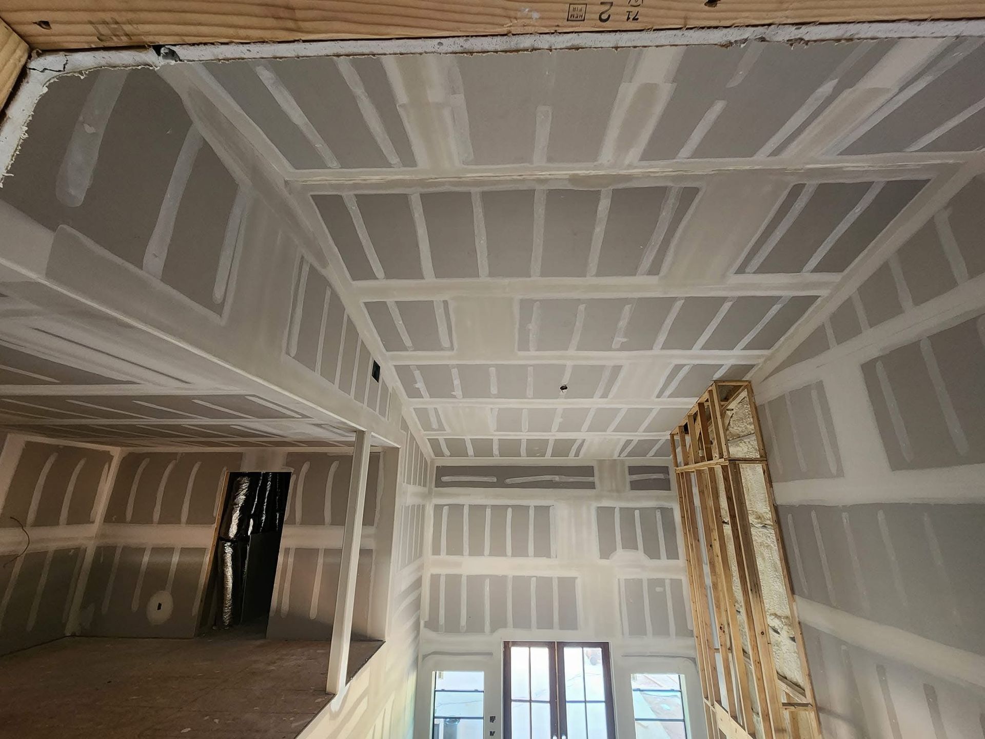 Interior view of a house under construction with drywall installed on walls and ceiling.