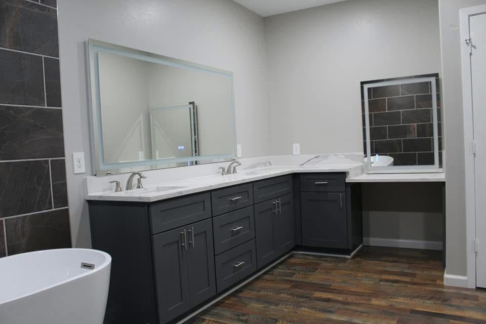 Bathroom with dark gray vanity, white countertops, large mirror, and wood-look flooring.
