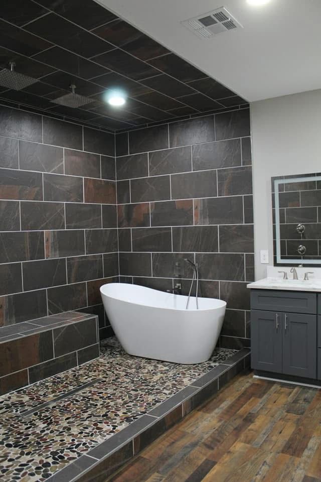 Modern bathroom with a freestanding tub, stone shower, and wooden flooring.