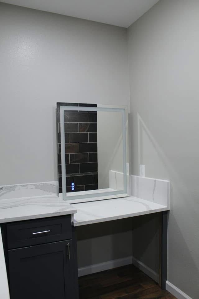 Vanity with a lit mirror on a gray counter, gray cabinets, and dark wood flooring.