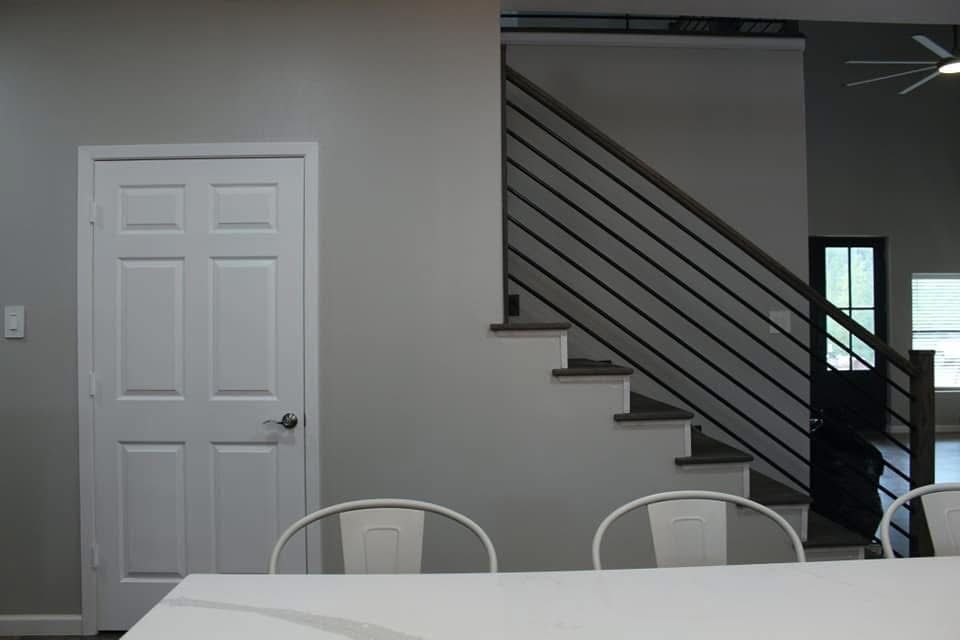 White door, stairs, and modern metal railing in a grey-walled interior with white chairs around a table.