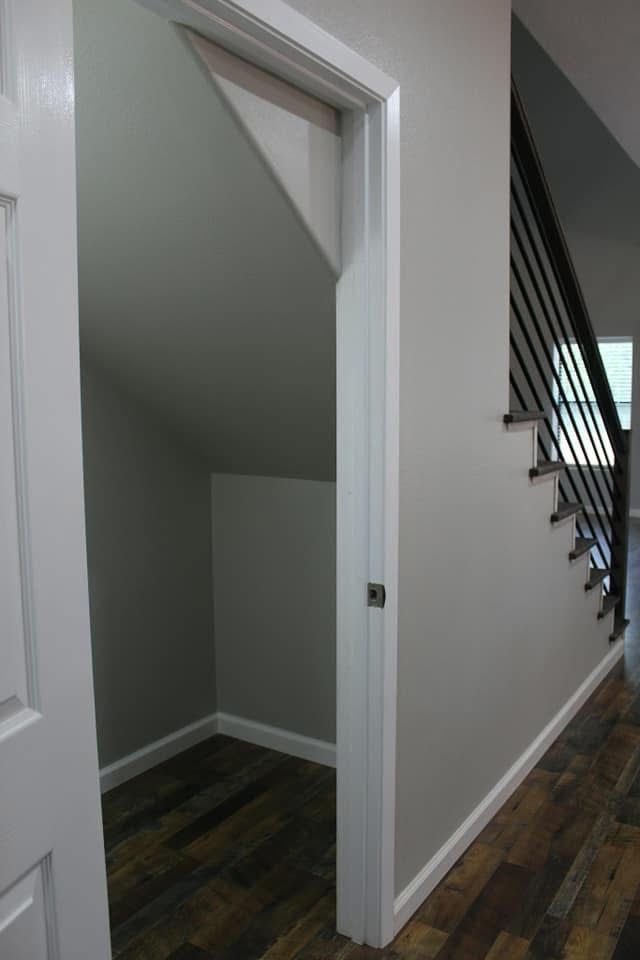 Storage closet under stairs with white door frame, wooden floor, and a staircase.