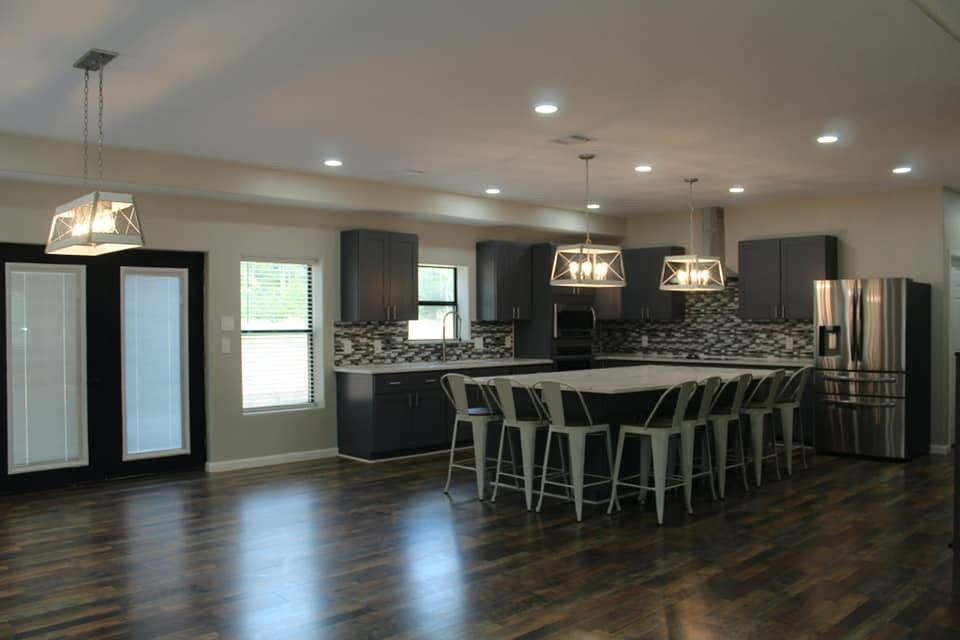 Modern kitchen with dark gray cabinets, large island with stools, and pendant lights.