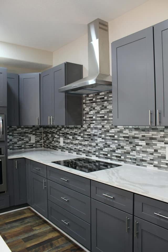 Gray kitchen with stainless steel vent hood, gray cabinets, and multi-colored mosaic backsplash.