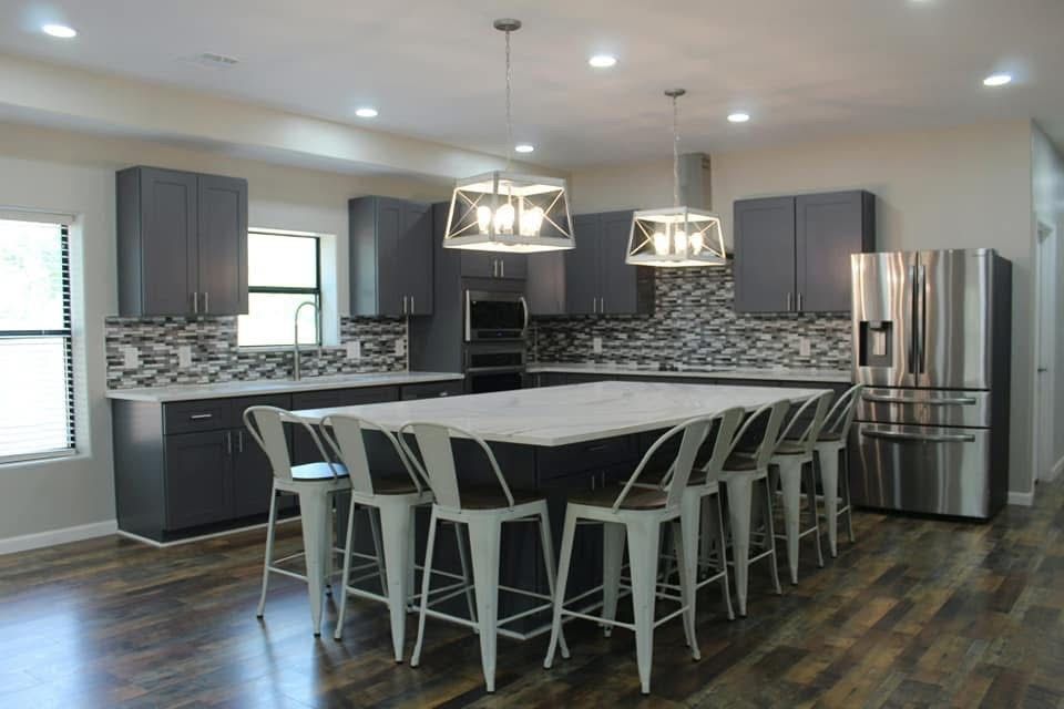Modern gray kitchen with island and white stools, stainless steel fridge, and wooden floors.