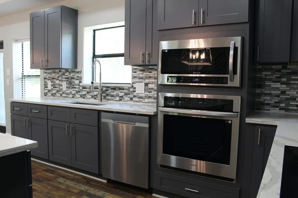 Gray modern kitchen with stainless steel appliances, dark cabinets, and marble countertops.