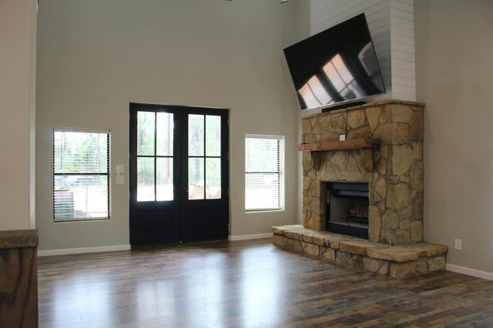 Living room with stone fireplace, large TV, black double doors, and windows.